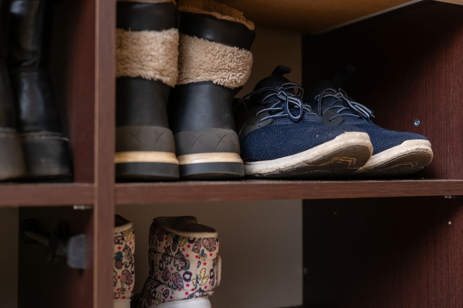 Different types of shoes, including boots and sneakers, are organized on a wooden shelf, creating a tidy and inviting entryway atmosphere