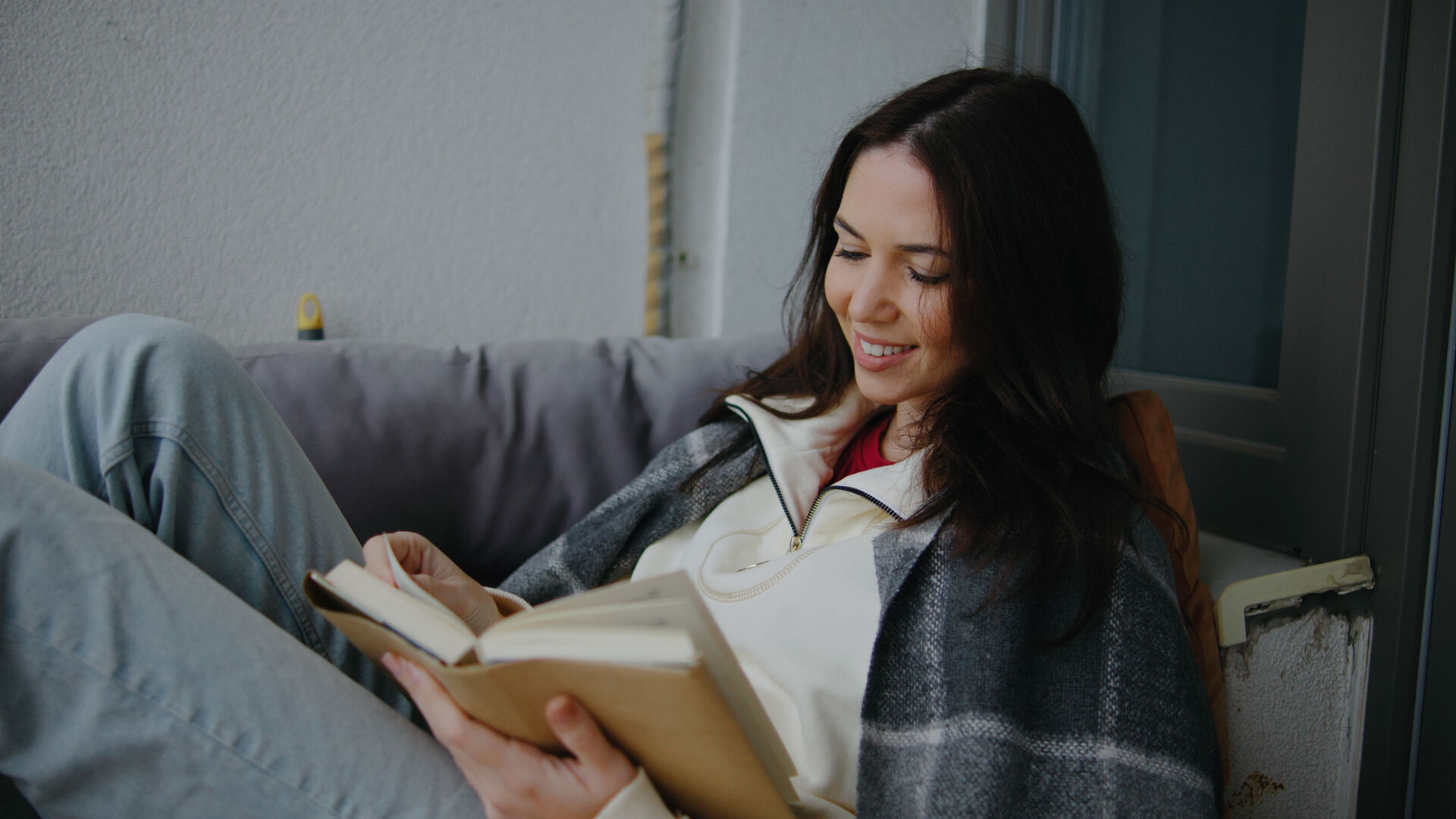 Woman reading a book comfortably while sitting on a cozy sofa in a bright indoor space during daytime
