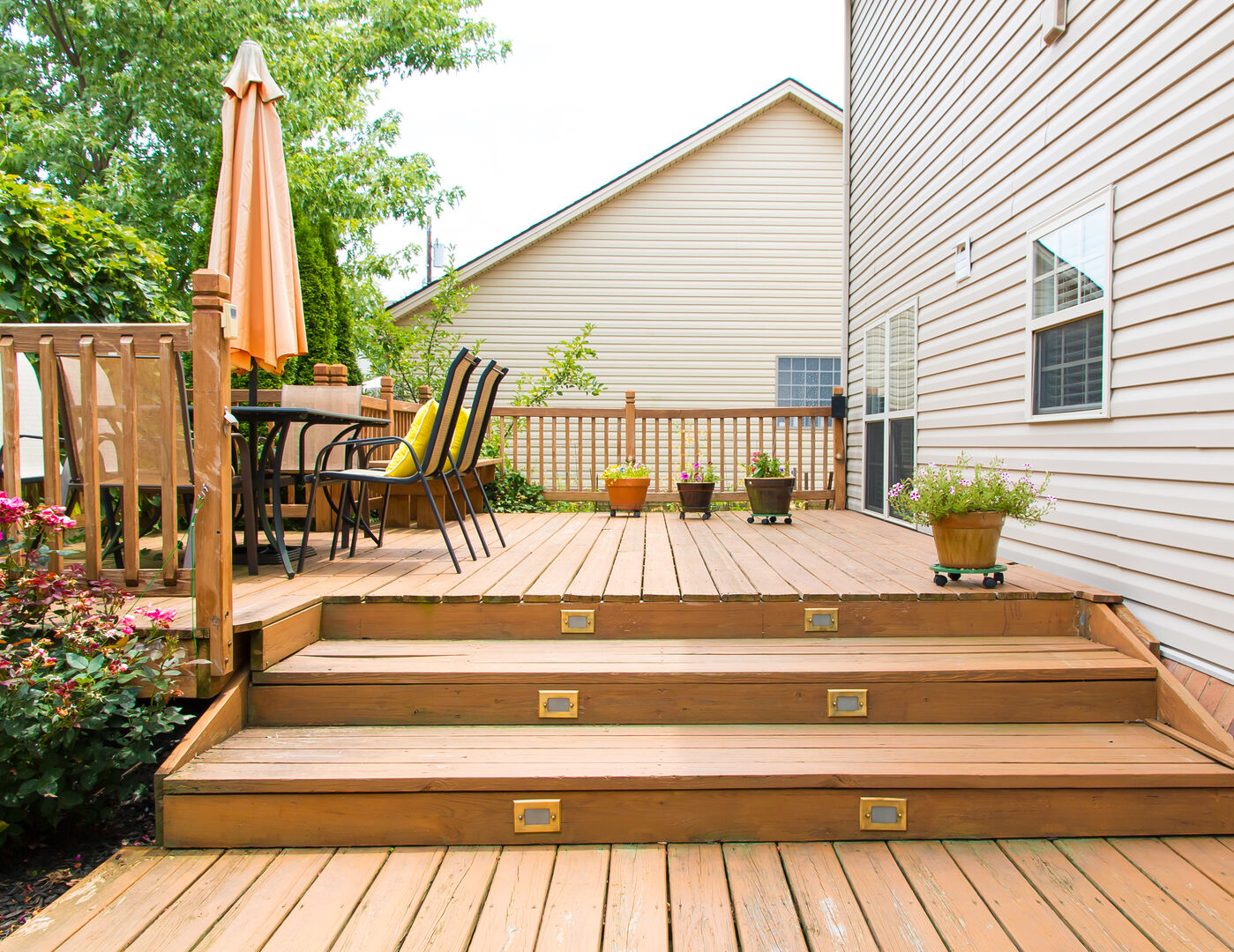 Large tan wood deck in backyard with greenery and lighting in deck staircase