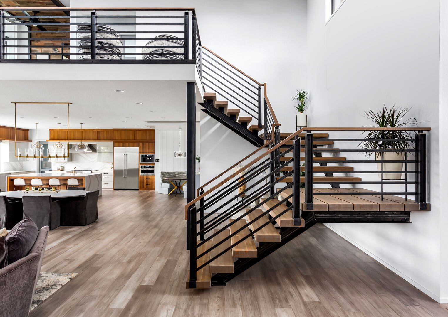 Open concept living room in new luxury home with modern industrial floating staircase and view of kitchen with large island and stainless steel appliances