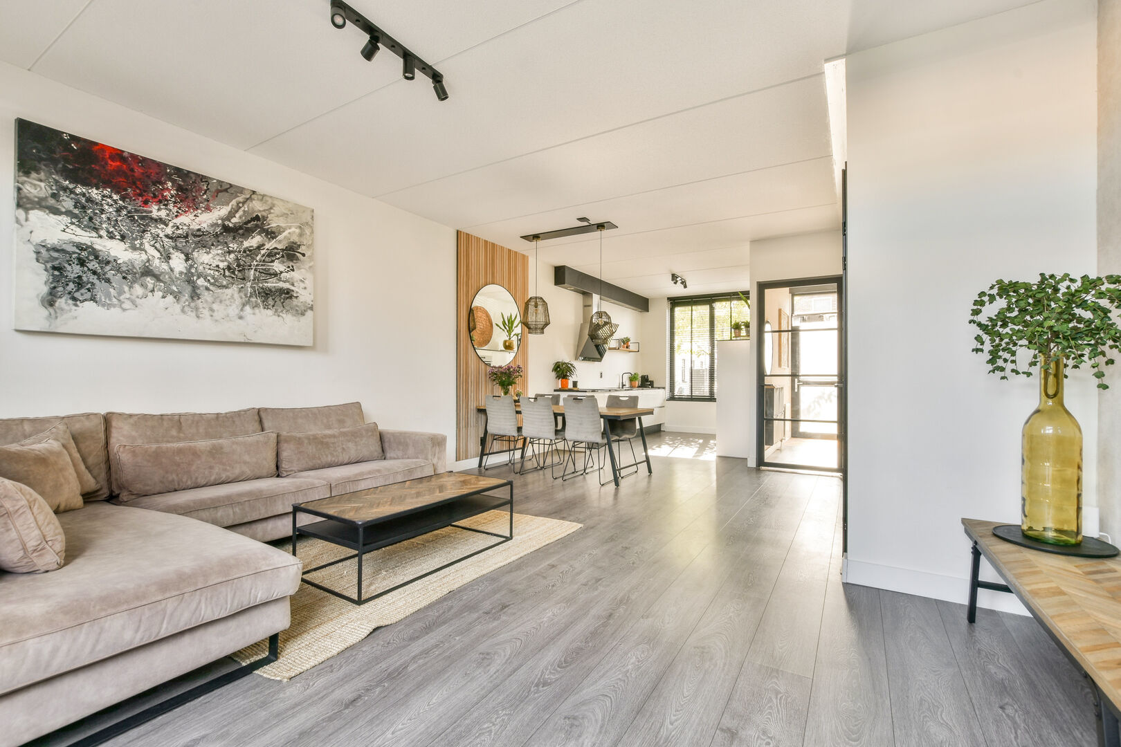 Modern open concept living room featuring a comfortable sofa, elegant artwork, and a bright dining area with slat wall feature