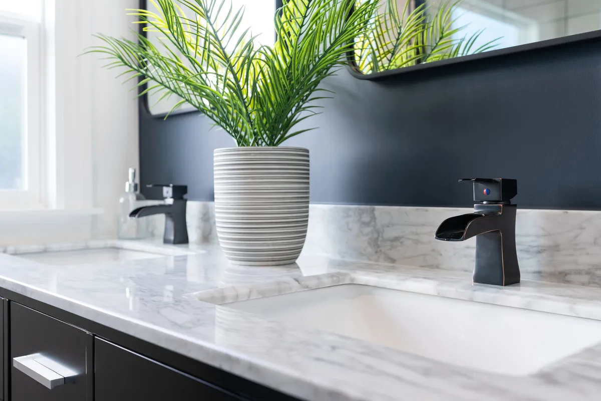 Close up of a black and white bathroom with double vanity sink in white and gray marble and dark grey walls