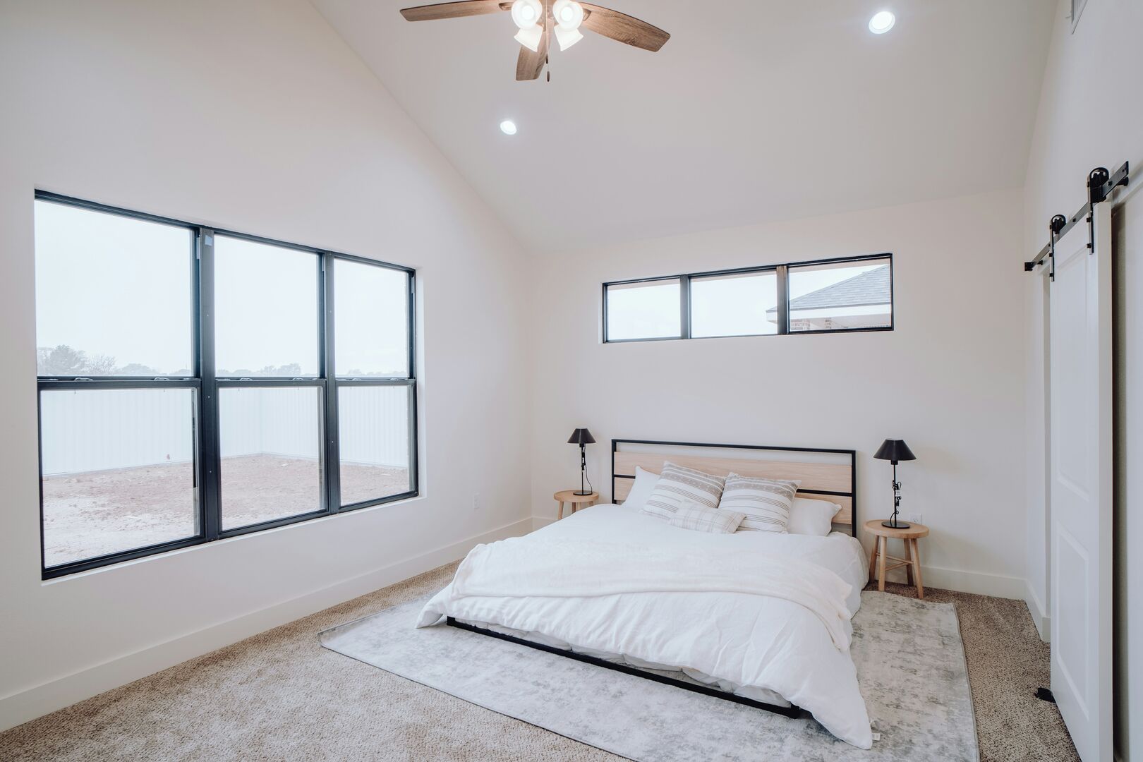 A minimalist bedroom with queen sized bed, white bedding and a tall white sliding door on a black metal track.