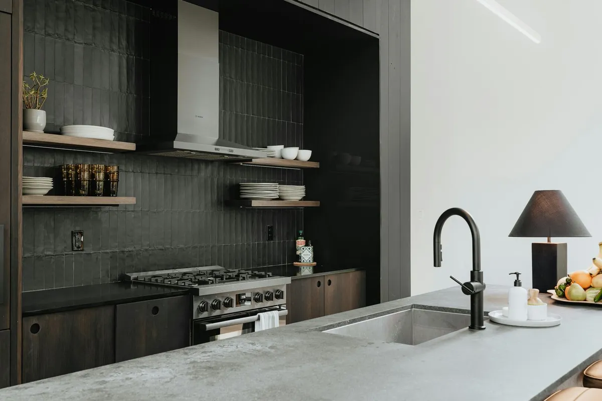 Dark industrial style galley kitchen with black backsplash and stainless steel appliances.