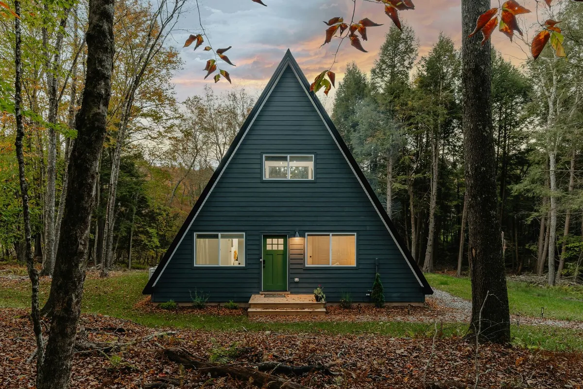 A-frame wood tiny home with blue exterior siding, black trim and a green exterior door.