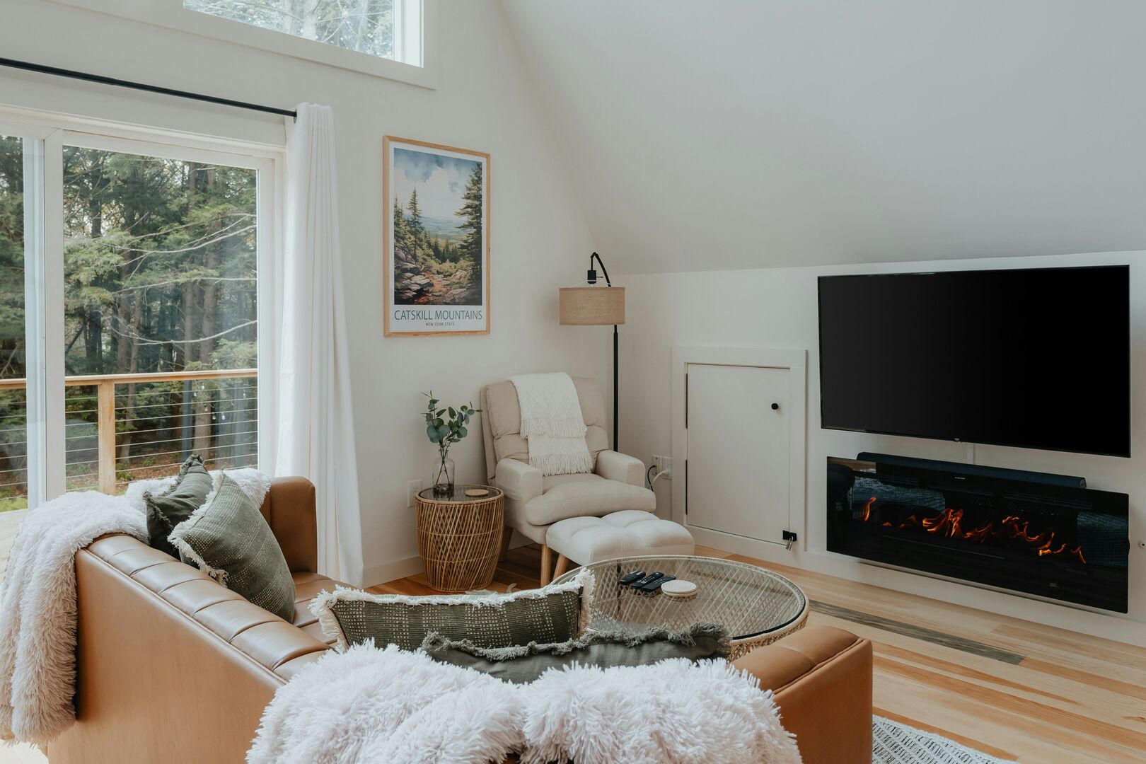 A small cabin with a beige reading chair, brown leather sofa, white fuzzy blankets and green toned throw pillows that make the living room very inviting.