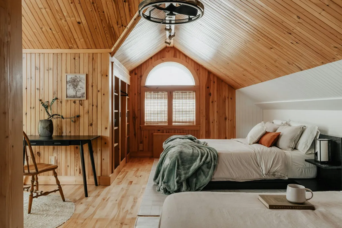 Modern cabin with rustic wood wall paneling and two queen beds with white linen bedsheets.