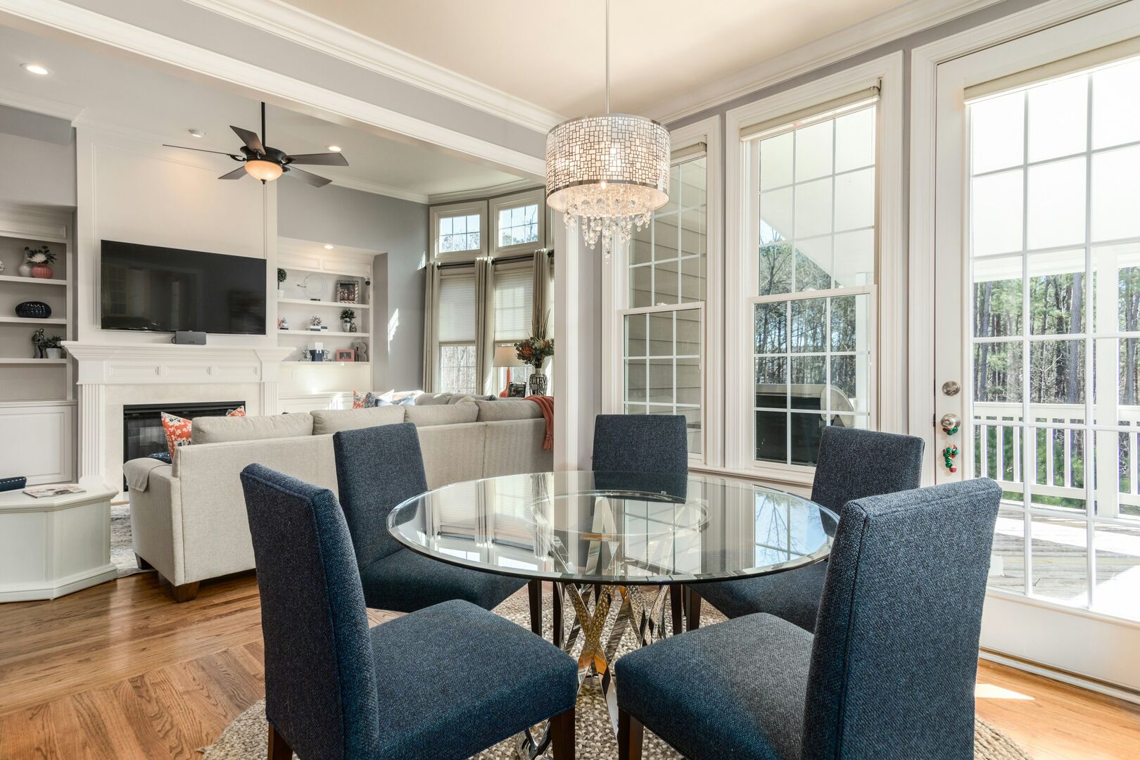 Large dining room with a crystal chandelier above blue dining room chairs and a glass table