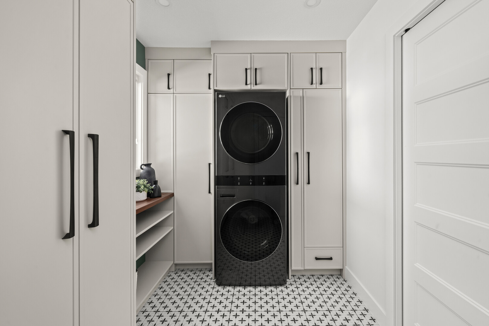 Laundry room with stacked black washer and dryer, white cabinetry, and patterned tile floor