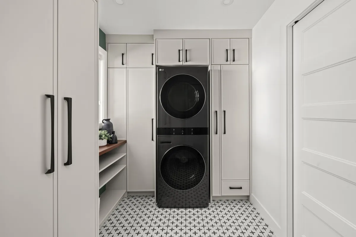 Laundry room with stacked black washer and dryer, white cabinetry, and patterned tile floor