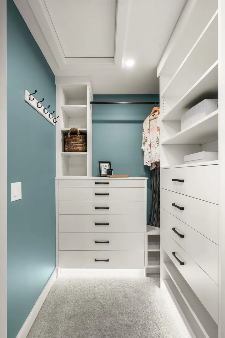 Walk-in closet with white drawers, open shelving, and teal walls