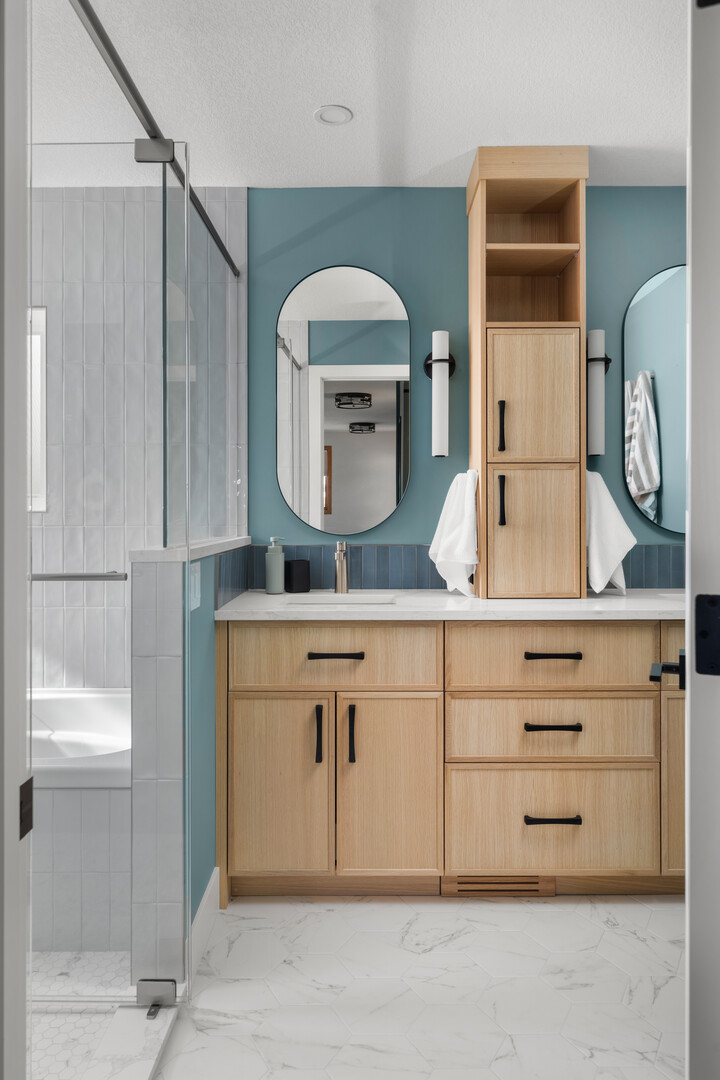 Light wood double vanity with blue walls and tall center storage cabinet