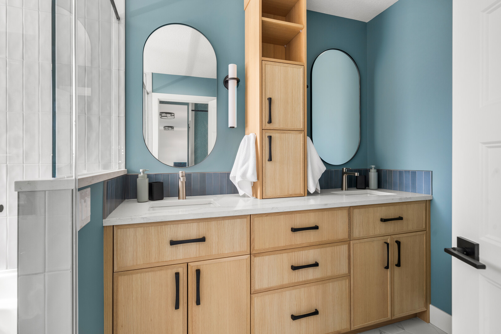 Double bathroom vanity with oval mirrors, blue walls, and black hardware