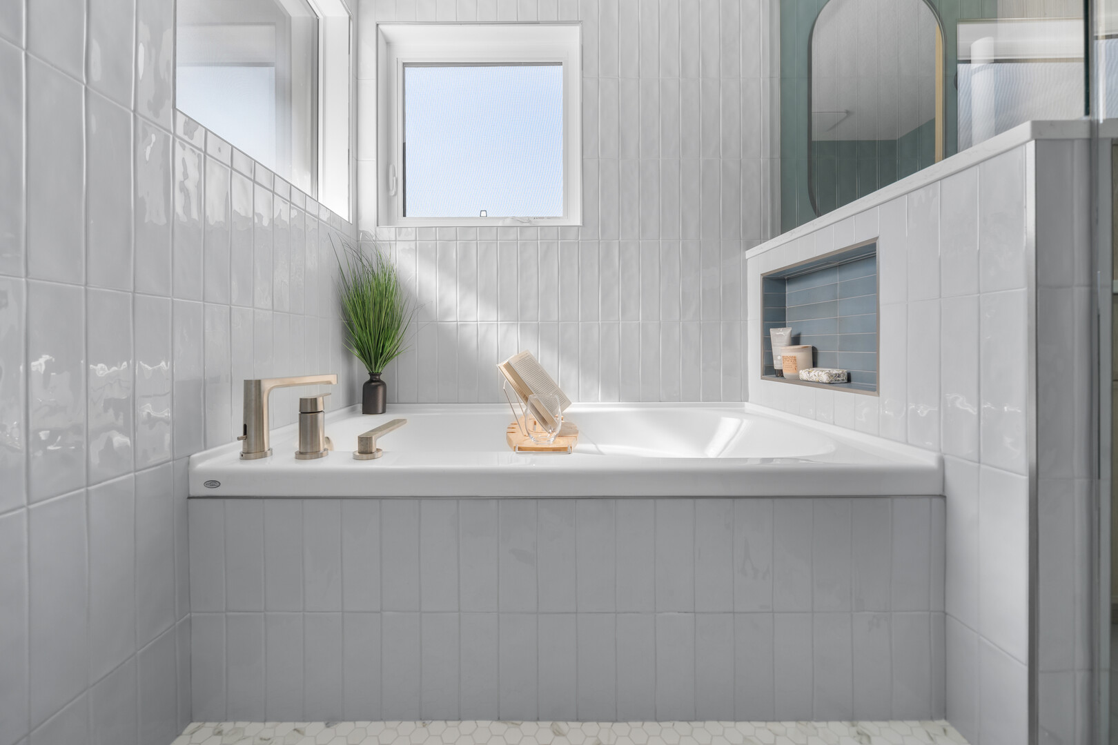 White tiled bathtub with brushed nickel faucet and built-in shower niche