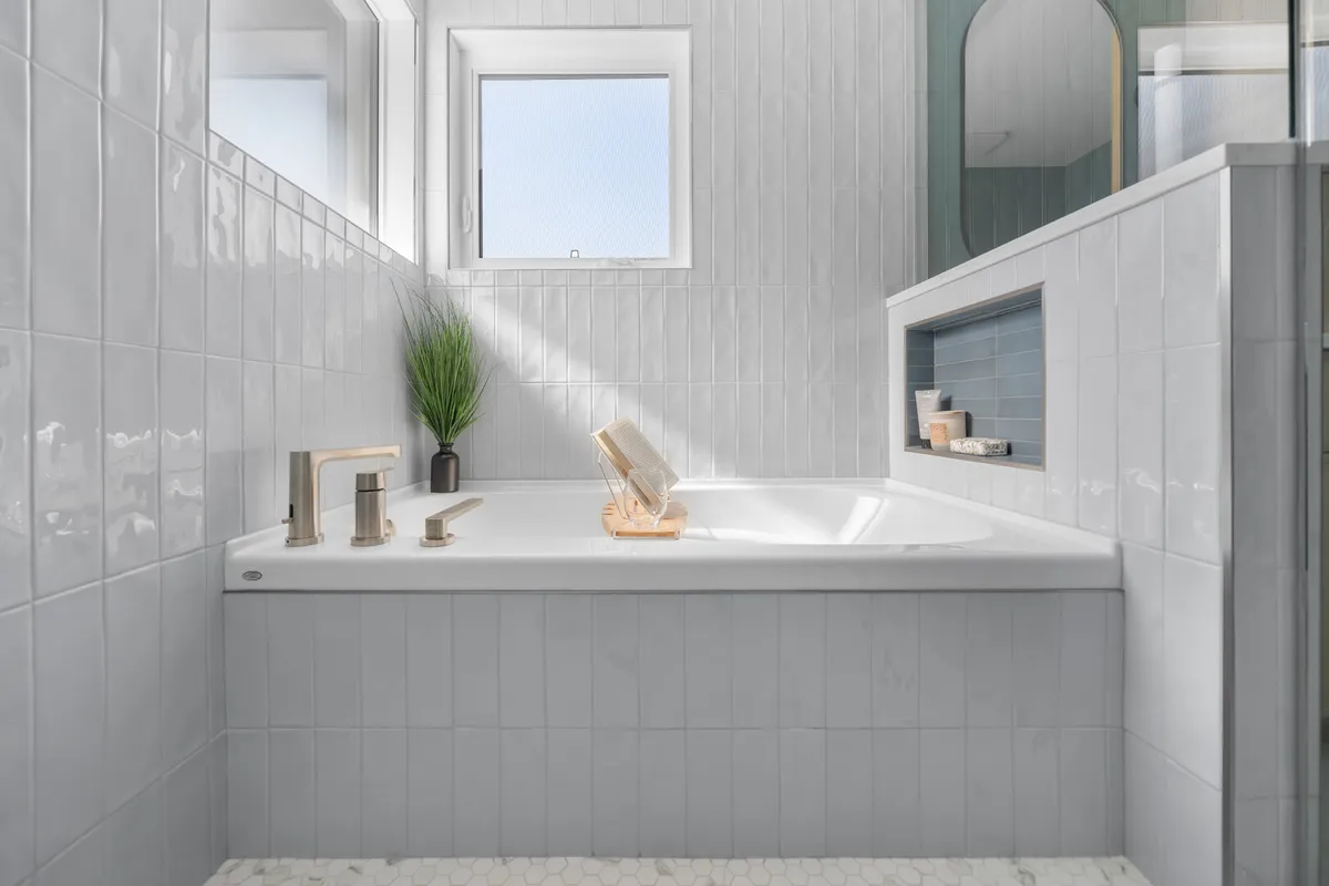 White tiled bathtub with brushed nickel faucet and built-in shower niche