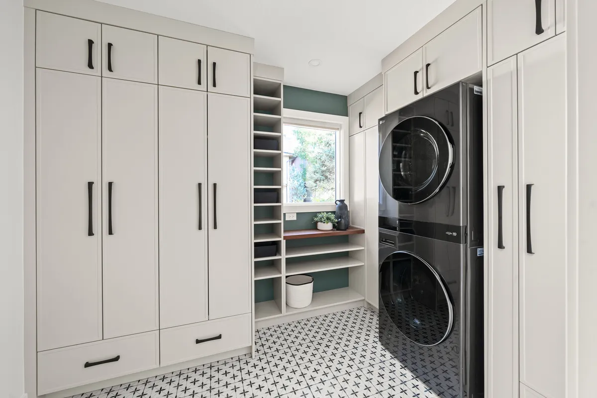 Mudroom and laundry room with white cabinetry, stacked black washer and dryer, and patterned tile floor