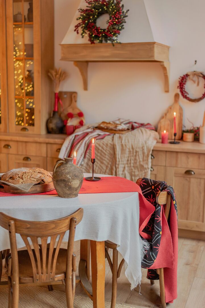 A kitchen with a wood dining table covered in a white tablecloth with red candlestick decor and a freshly baked loaf of bed.