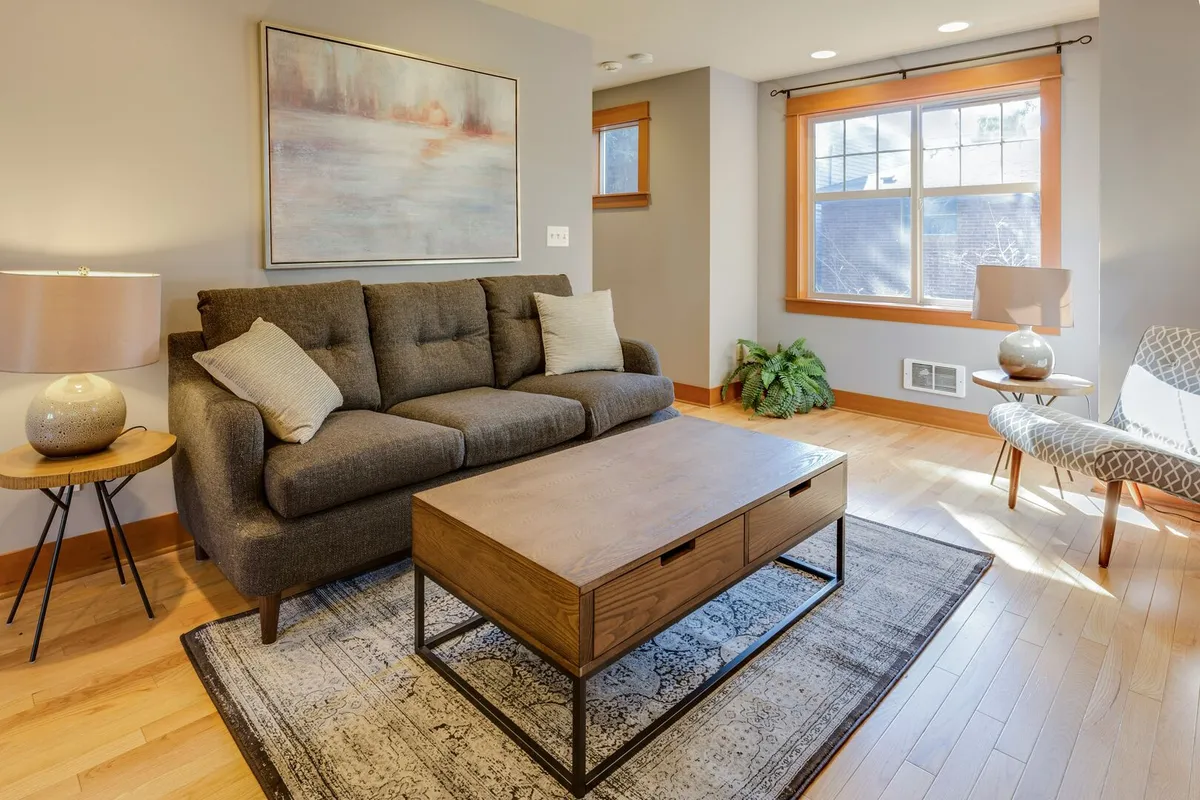 Small living room with a large window, dark grey couch, and a wood coffee table on black metal legs with drawer storage. 
