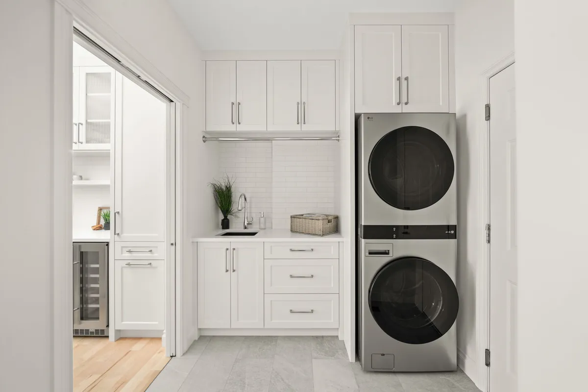 Laundry room with stacked washer and dryer, black sink, and white cabinetry