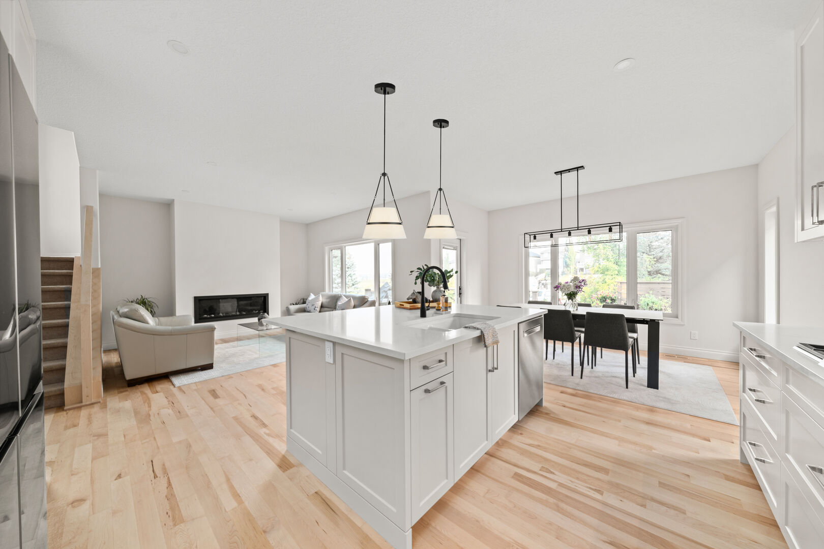 Open-concept white kitchen with a large island, dining area, and living room fireplace