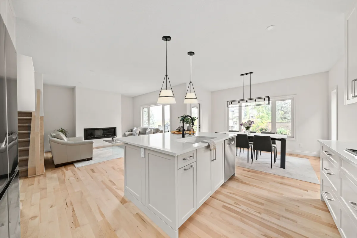 Open-concept white kitchen with a large island, dining area, and living room fireplace