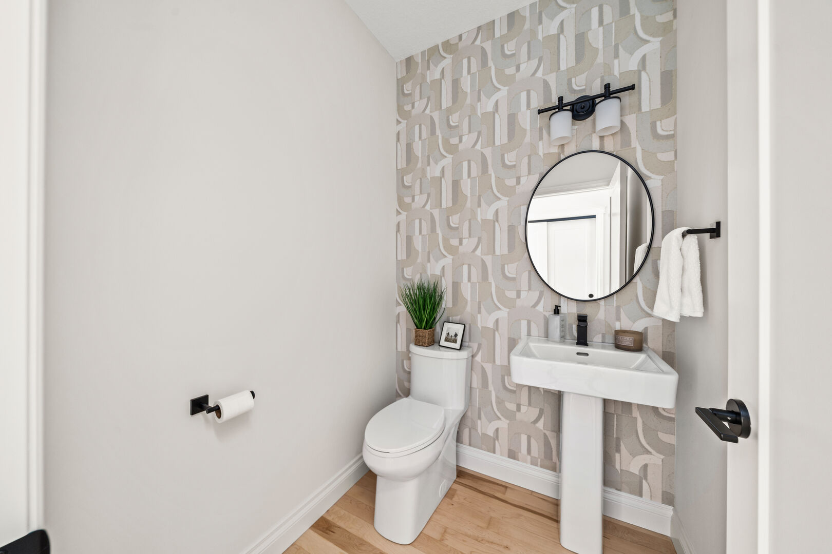 Powder room with geometric wallpaper, pedestal sink, and round mirror