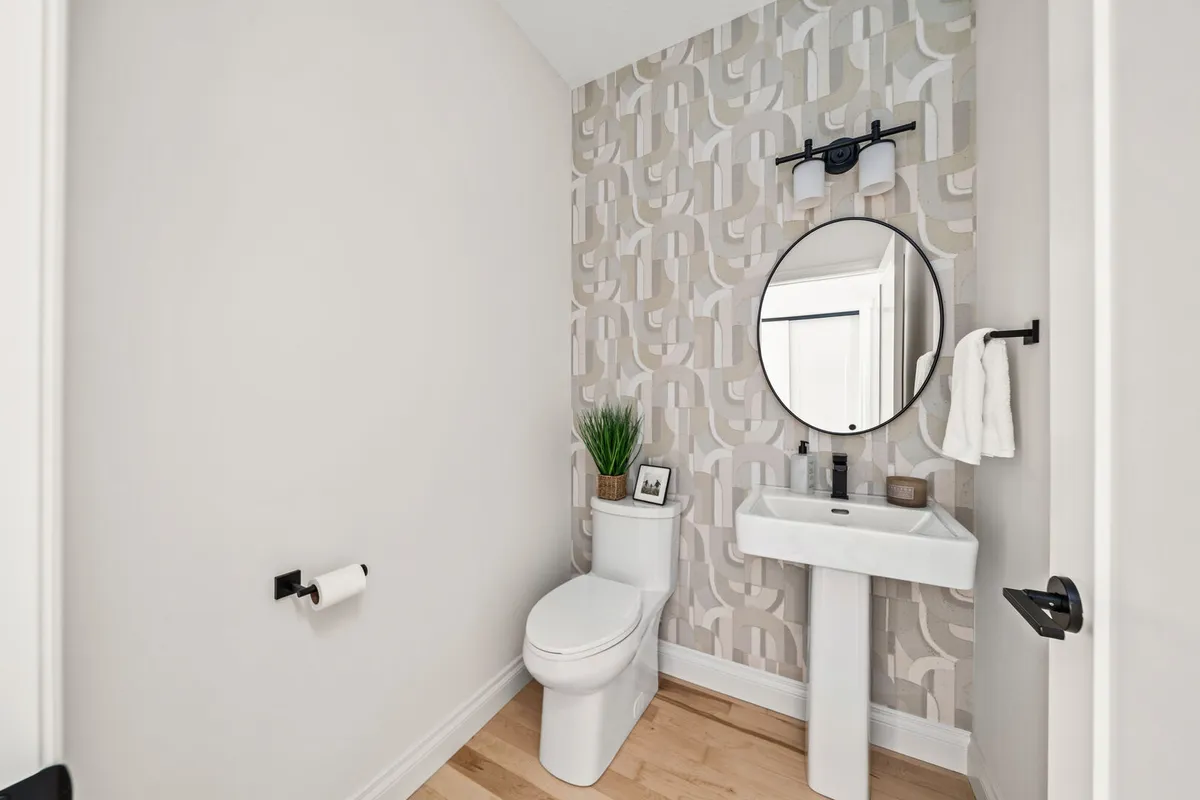 Powder room with geometric wallpaper, pedestal sink, and round mirror