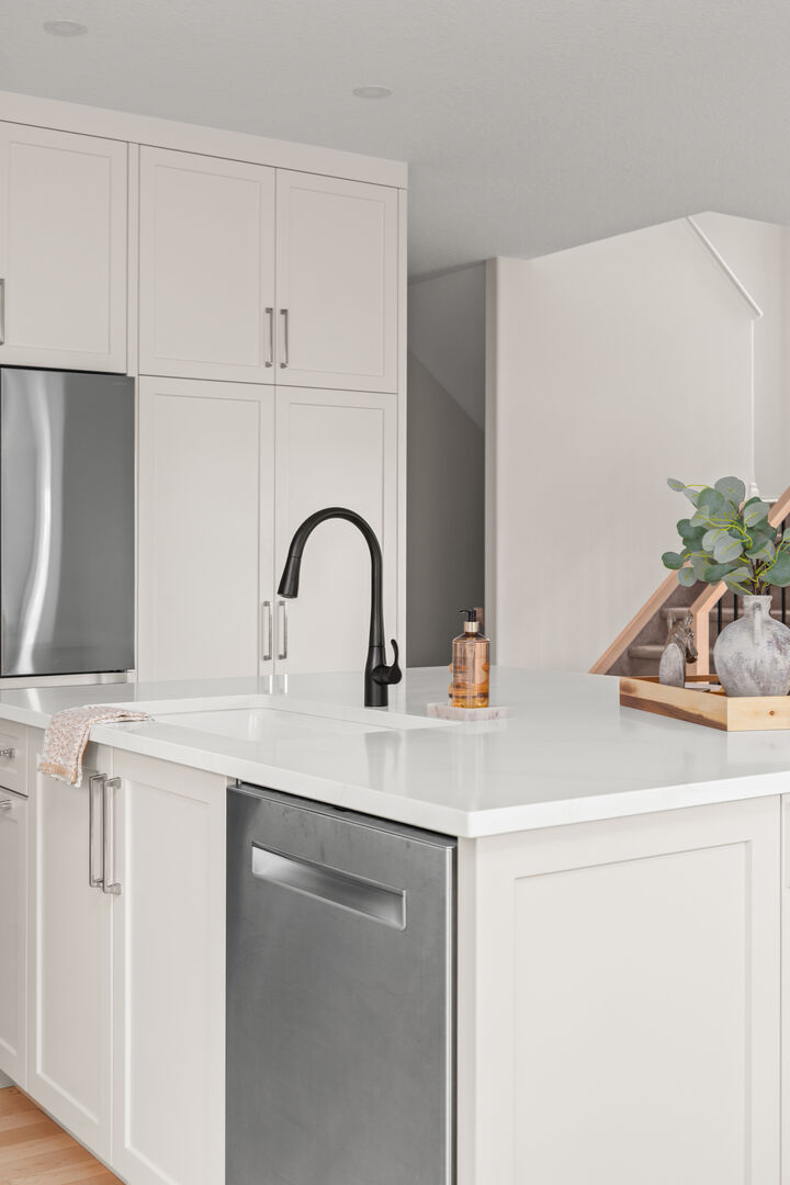 White kitchen with a large island, dining table, and stainless refrigerator