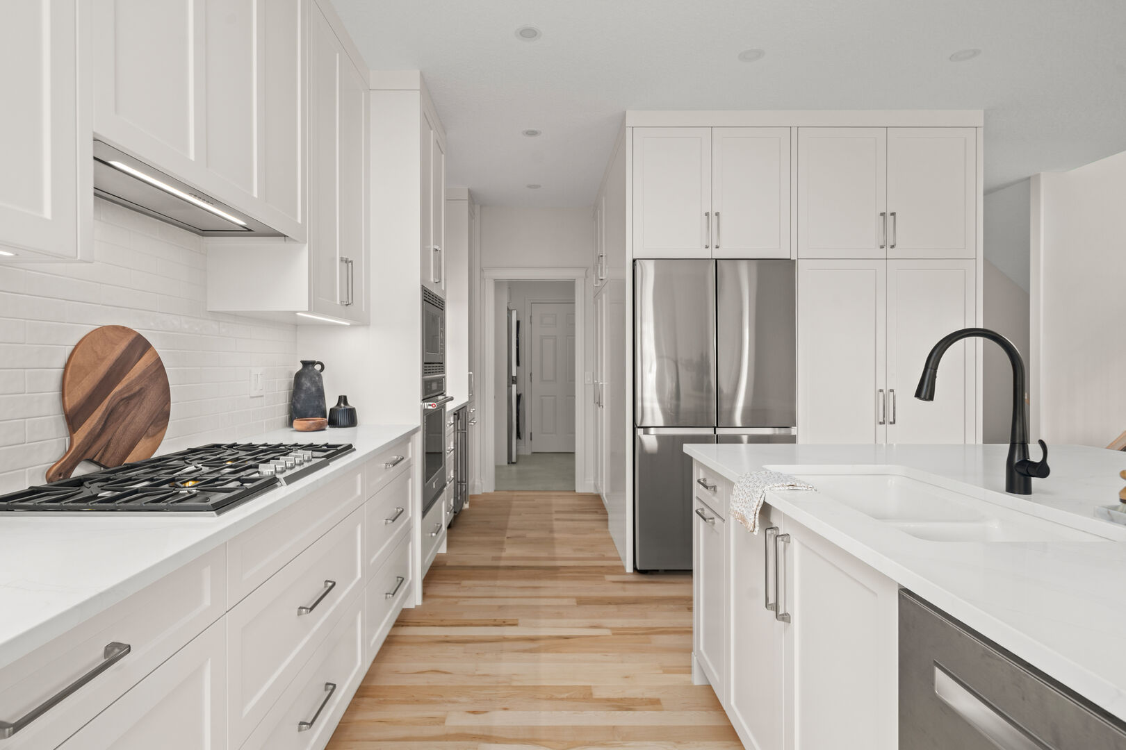Galley view of a white kitchen with a gas cooktop and island sink