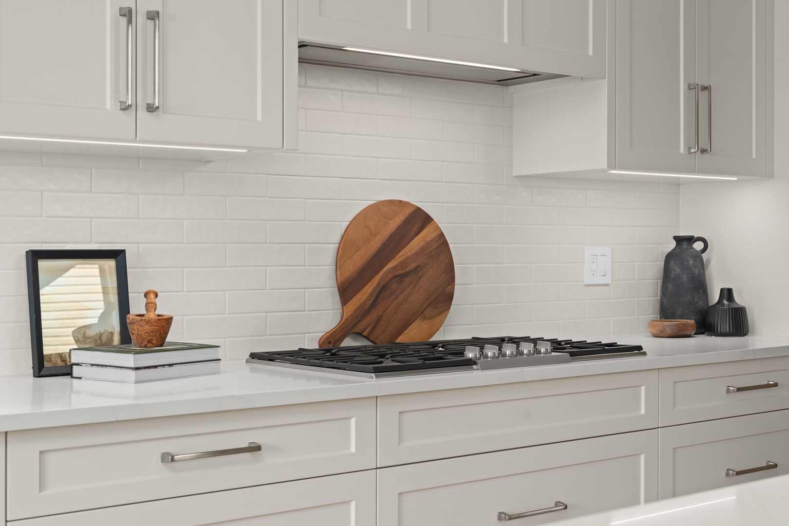 White kitchen cooktop with subway tile backsplash and wood cutting board