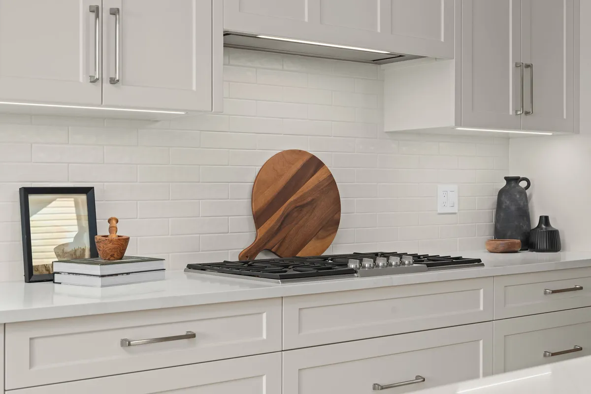White kitchen cooktop with subway tile backsplash and wood cutting board