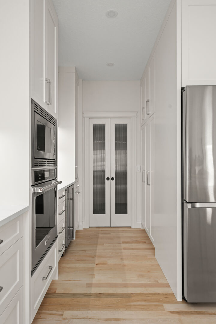 Butler's pantry corridor with built-in ovens and reeded glass double doors