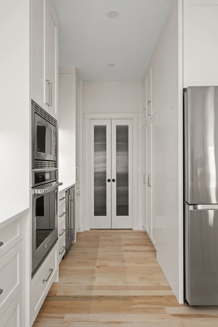 Butler's pantry corridor with built-in ovens and reeded glass double doors