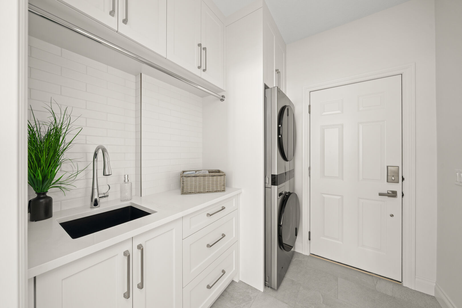 Laundry room with a black sink, stacked washer and dryer, and garage entry door