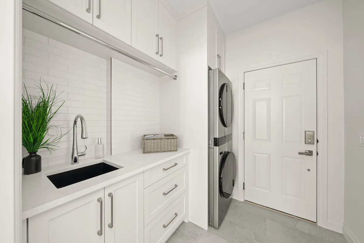 Laundry room with a black sink, stacked washer and dryer, and garage entry door