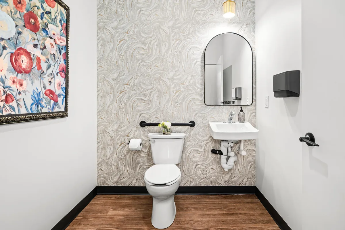 Black and white commercial bathroom with marble look wallpaper and black and gold accents