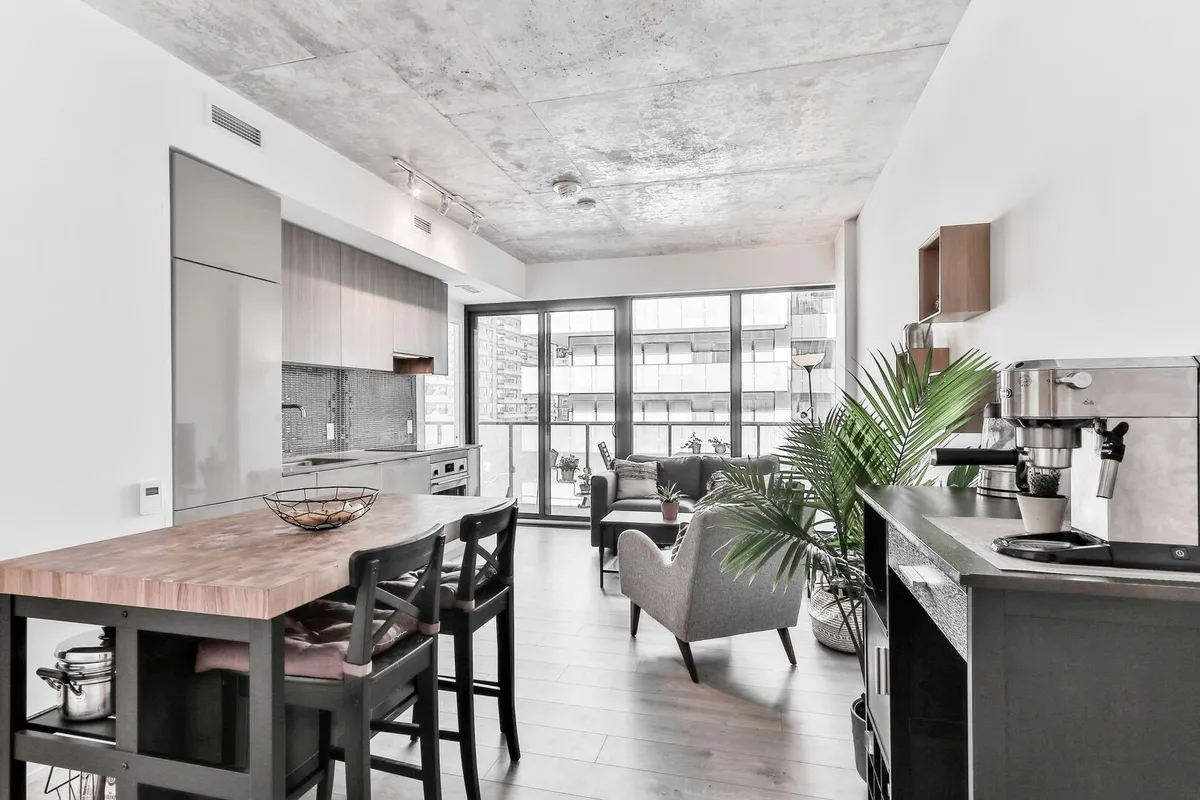 Brown wood table in an open-concept industrial style living room with a grey sitting chair facing large windows.