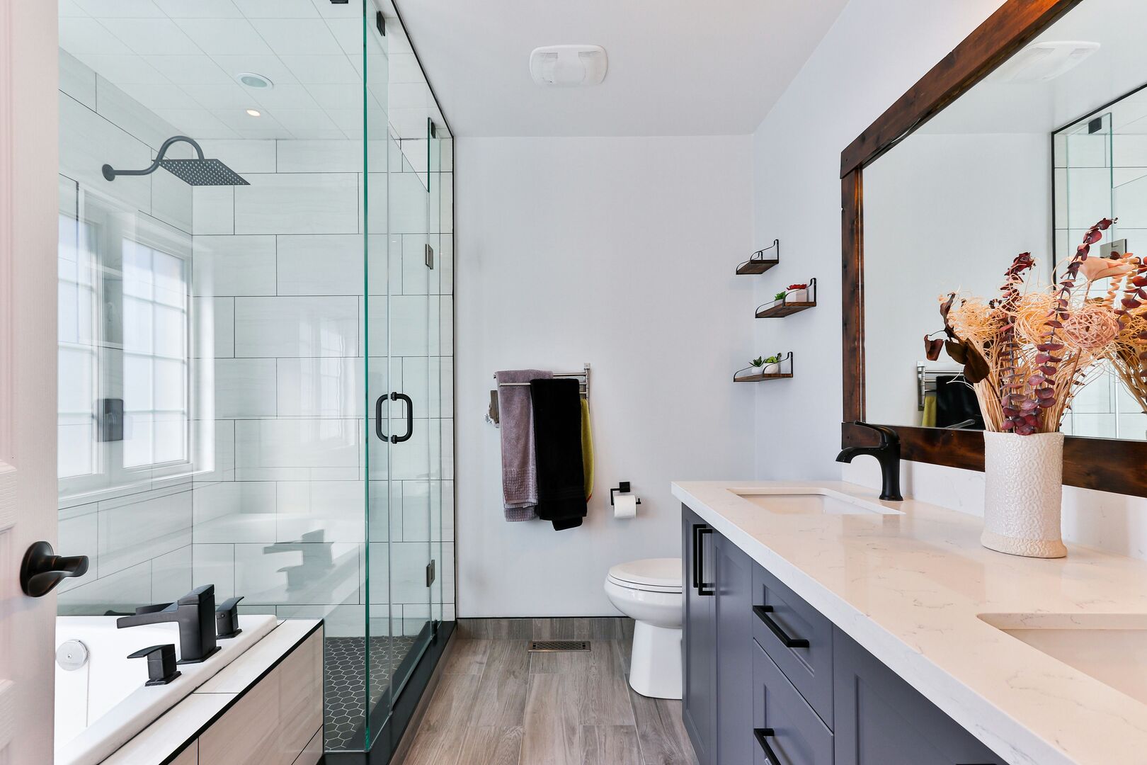 Modern farmhouse bathroom with wood floors, white walls and charcoal vanity.
