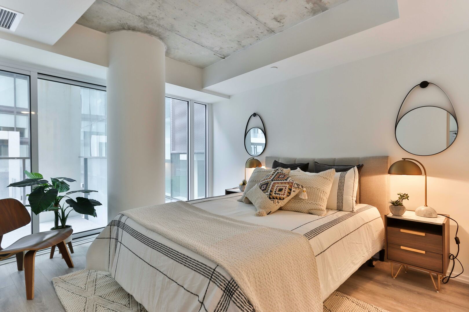 Apartment bedroom with white and black linen bed sheets, walnut wood side chair and side tables.