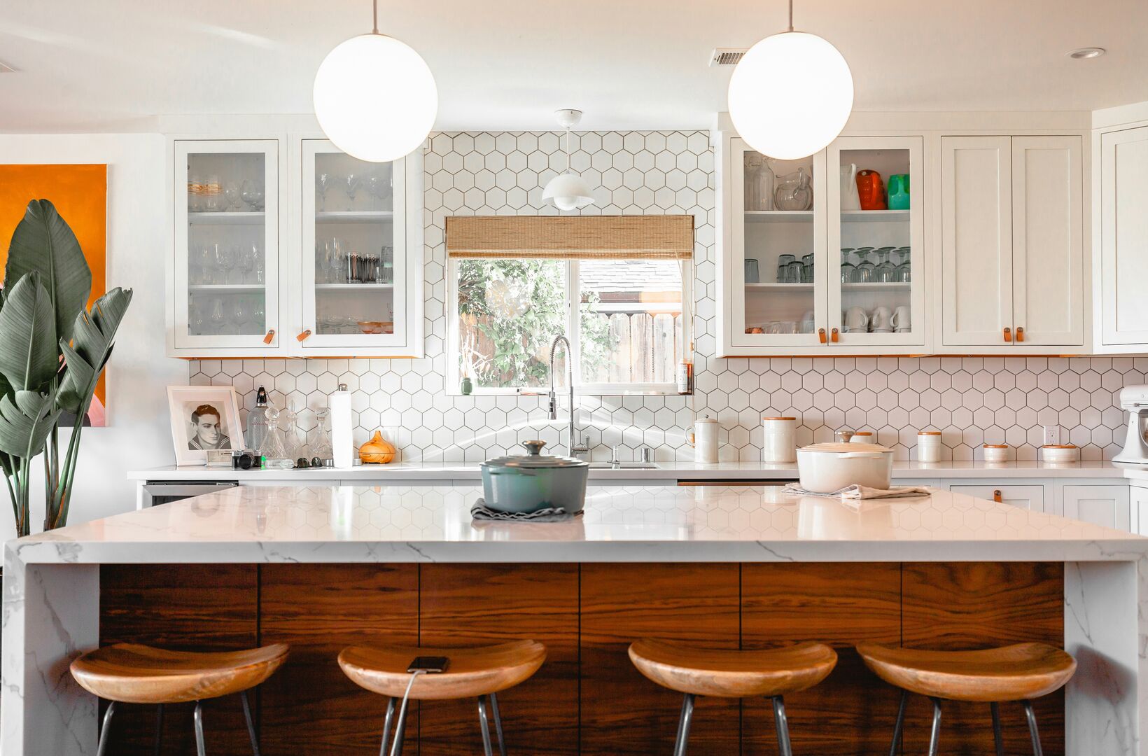 Light and bright kitchen with wood cabinetry and wood counter stools with white upper cabinets and modern white hexagonal wall tile.