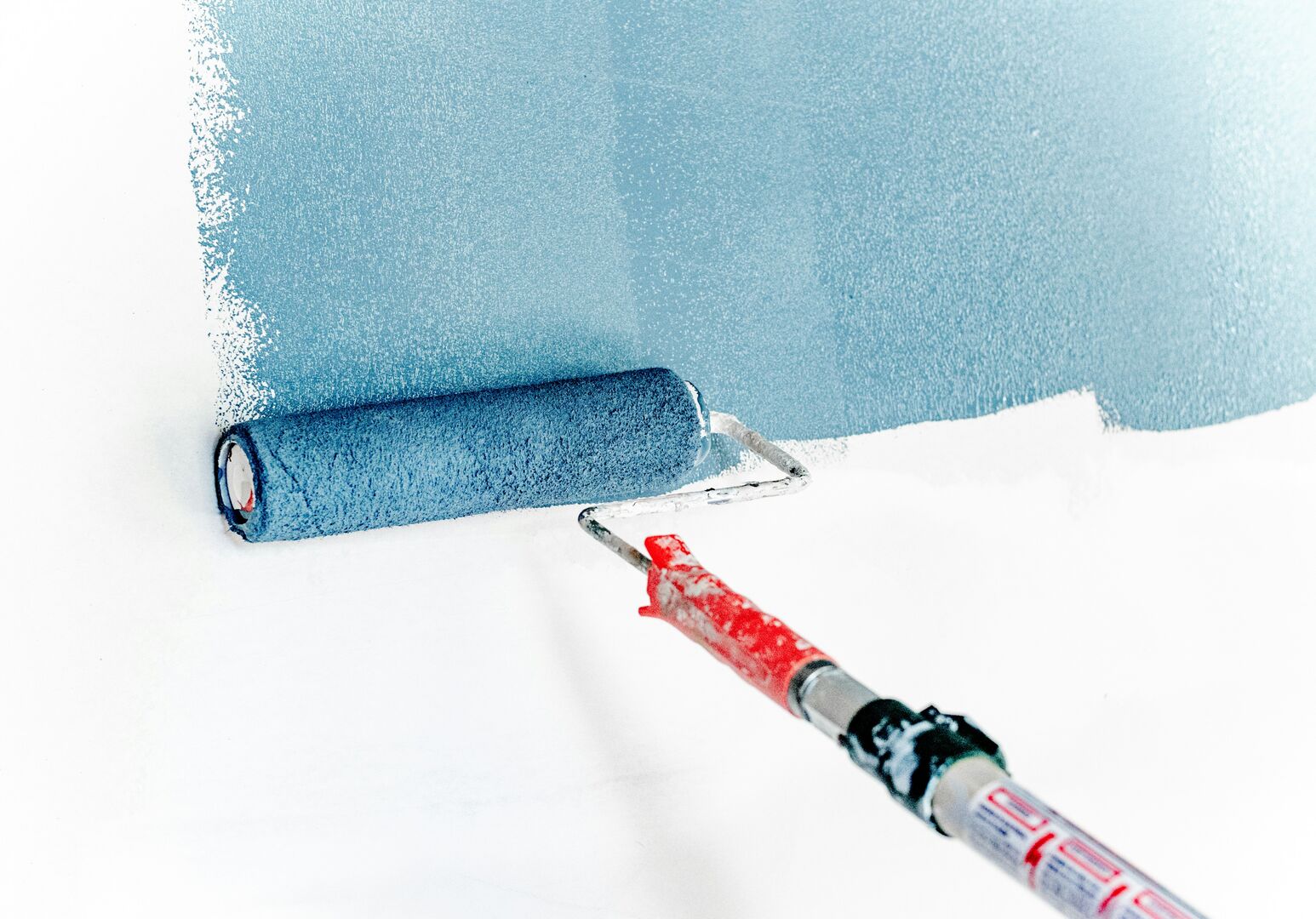 Blue wall paint being applied with a large roller on a wall.