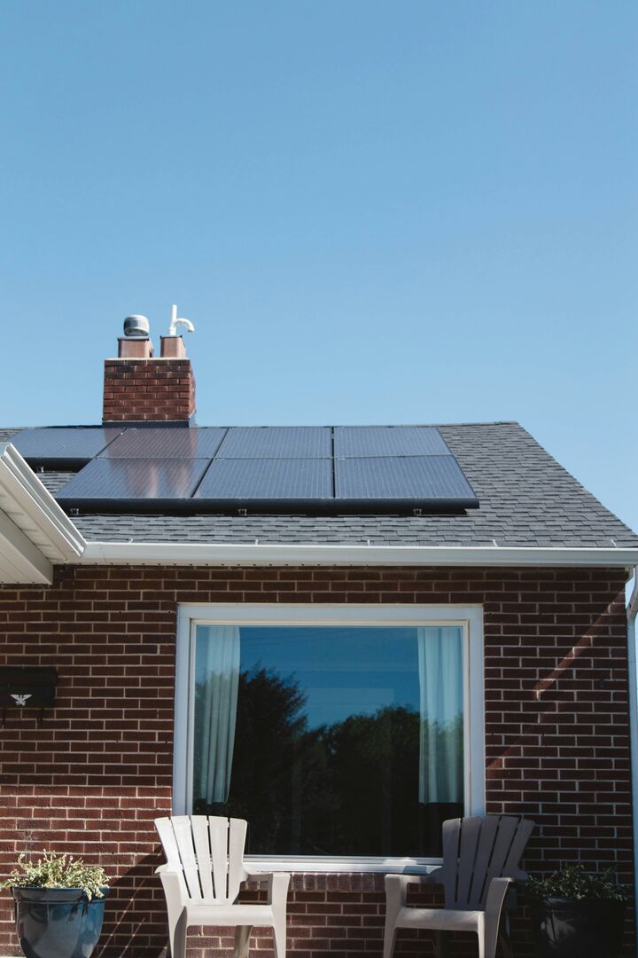 Exterior view of a brown brick home with solar panels on top of the roof shingles.