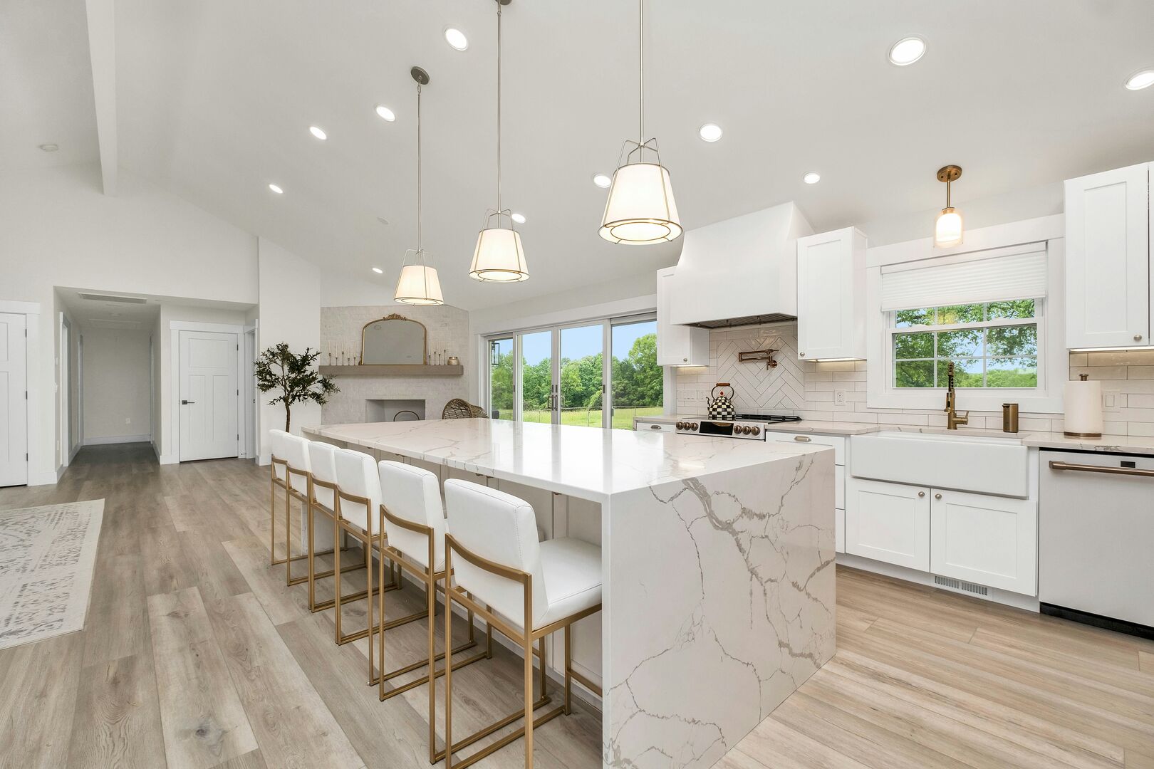 A large kitchen with white cabinetry and an island with a marble countertop that has a waterfall edge.