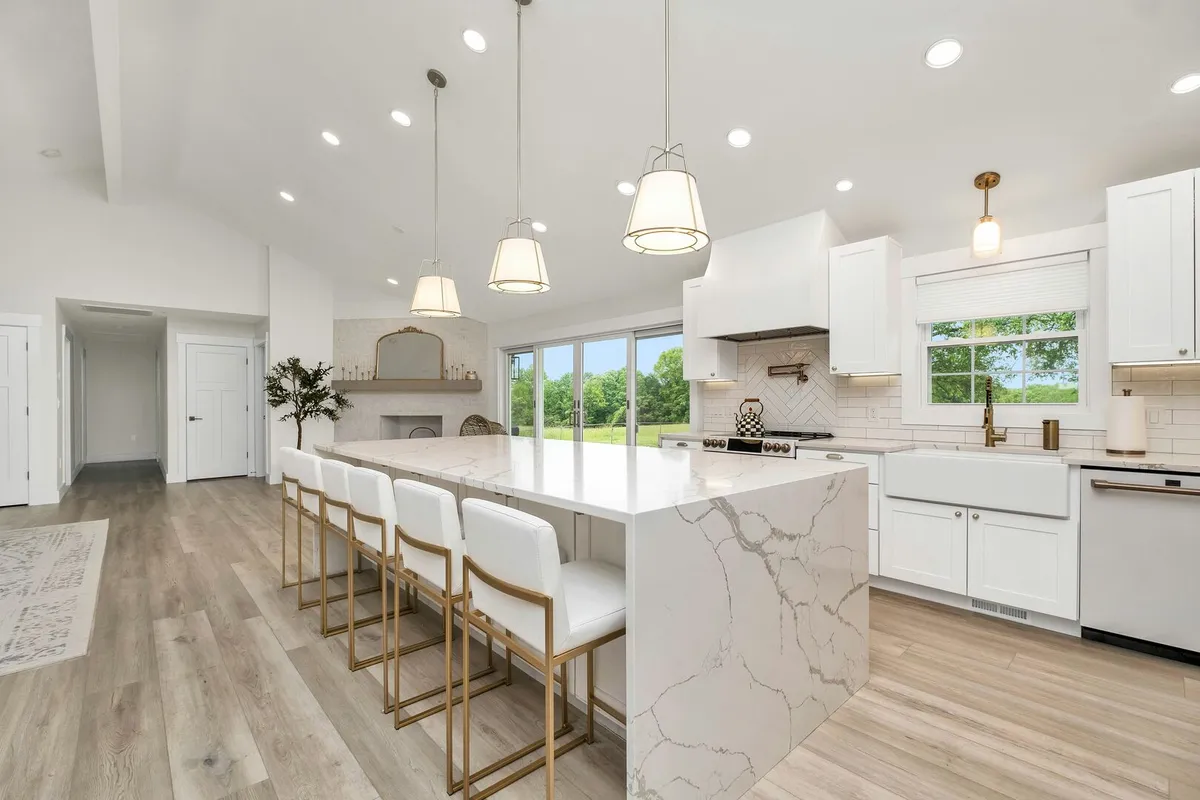 A large kitchen with white cabinetry and an island with a marble countertop that has a waterfall edge.